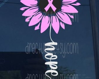 Könnte beinhalten: Pinkfarbene Sonnenblume mit einem rosa Band in der Mitte und dem Wort "Hope" in kursiv darunter geschrieben.