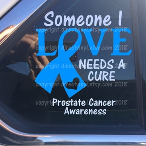 May include: Blue ribbon with a heart and the text "Someone I Love Needs a Cure Prostate Cancer Awareness" on a car window.