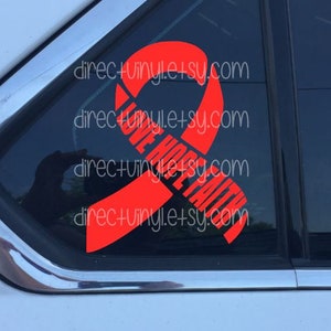 Può includere: Nastro rosso con le parole "Love Hope Faith" su un finestrino di un'auto nera.