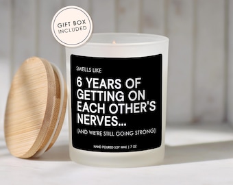 May include: A frosted glass candle with a black label featuring the white text: SMELLS LIKE 6 YEARS OF GETTING ON EACH OTHER'S NERVES... (AND WE'RE STILL GOING STRONG) HAND POURED SOY WAX | 7 OZ. A round bamboo lid sits beside the candle, and a circular tag reads GIFT BOX INCLUDED.