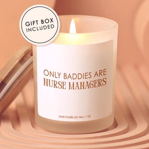 May include: A lit, frosted glass candle with the text "ONLY BADDIES ARE NURSE MANAGERS" in brown. The candle has a wooden lid and is labeled "HAND POURED SOY WAX | 7 OZ". A "GIFT BOX INCLUDED" sticker is visible.