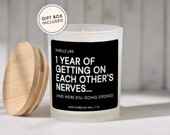 May include: A white candle with a wooden lid, featuring a black label with the text "Smells Like 1 Year of Getting on Each Other's Nerves..." and "Hand Poured Soy Wax | 7 oz". A gift box is included.