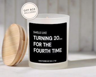 May include: A white frosted glass candle with a black label that reads "Smells Like Turning 20... For The Fourth Time." The candle has a wooden lid and is labeled "Hand Poured Soy Wax | 7 oz." A gift box is included.