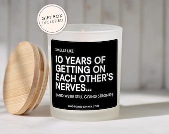 May include: A white frosted glass candle with a bamboo lid. The candle has a black label with white text that reads "Smells Like 10 Years of Getting on Each Other's Nerves..." and "Hand Poured Soy Wax | 7 oz". A gift box is included.