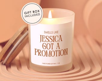 May include: A lit soy wax candle in a frosted glass jar with a wooden lid. The label reads "Smells Like Jessica Got a Promotion." The candle is 7 oz and comes in a gift box.