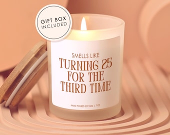 May include: A lit soy wax candle in a frosted glass jar with a wooden lid. The label reads "Smells Like Turning 25 For The Third Time." The candle is 7 oz and includes a gift box.