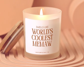 May include: A lit soy wax candle in a frosted glass jar with a wooden lid. The label reads "Smells Like World's Coolest Memaw." The candle is 7 oz.