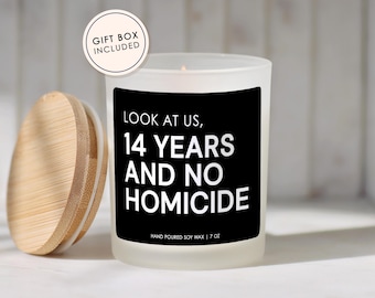 May include: A white candle with a black label that reads "LOOK AT US, 14 YEARS AND NO HOMICIDE." The candle has a wooden lid and a "GIFT BOX INCLUDED" sticker. The candle is 7 oz.