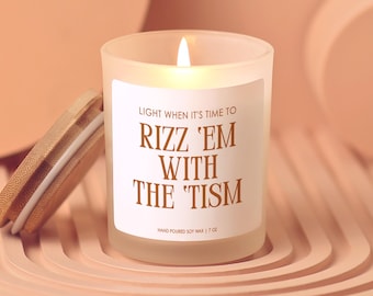 May include: A lit, frosted glass candle with a wooden lid. The candle has a white label with the text "LIGHT WHEN IT'S TIME TO RIZZ 'EM WITH THE 'TISM" in brown. The candle is hand-poured soy wax and weighs 7 oz.