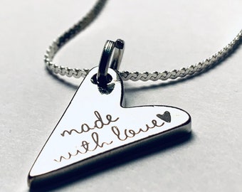 Könnte beinhalten: Eine silberne Halskette mit einem herzförmigen Anhänger, auf dem "made with love" steht.
