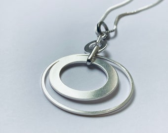 May include: A silver necklace with a pendant featuring two interlocking circles. The circles are smooth and have a brushed finish.