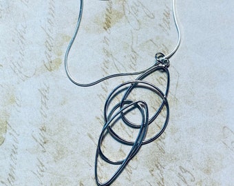 May include: A silver chain necklace with a pendant featuring an abstract design of overlapping circles and ovals.