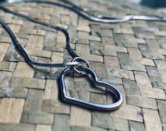May include: A silver chain necklace with a silver heart pendant. The heart pendant is open and has a smaller circle inside.