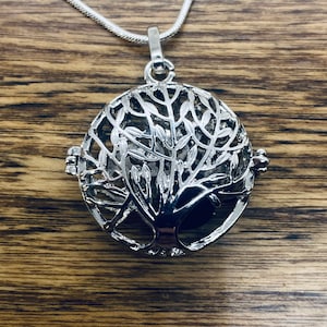 Könnte beinhalten: Silberne Baum des Lebens Anhänger Halskette mit einem runden, durchbrochenen Design. Der Anhänger ist an einer silbernen Kette befestigt.