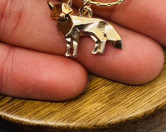 May include: A gold-toned necklace featuring a geometric fox pendant with sharp, angular facets. The fox charm is suspended from a delicate gold-colored chain, showcasing a polished metallic finish that reflects light across its structured, origami-inspired form.