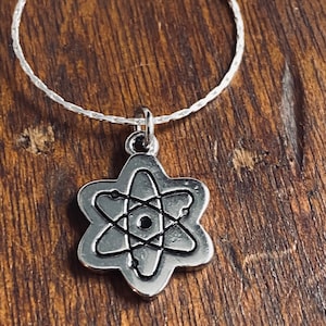 May include: A silver necklace with a silver atom charm. The atom charm has a black center and silver rings around it.