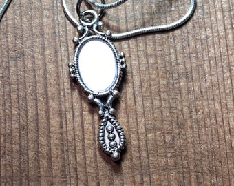 May include: A silver chain necklace with a silver hand mirror pendant. The mirror is oval shaped and has a decorative border.