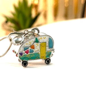 May include: A silver necklace with a colorful enamel camper charm. The camper is decorated with a mosaic pattern and has a yellow door and black wheels.