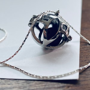 May include: A silver necklace with a cage-like pendant. The pendant is open and has a delicate design.