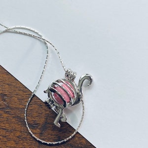 May include: A silver flamingo charm necklace with a pink pearl inside. The necklace is on a silver chain.