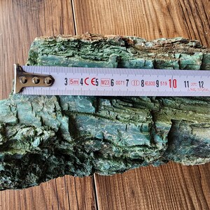 Op de afbeelding: Een stuk getextureerde, turquoise gekleurde schors met een meetlint eroverheen. De tape toont metingen in centimeters, waarbij de schors ongeveer 13 cm lang is.