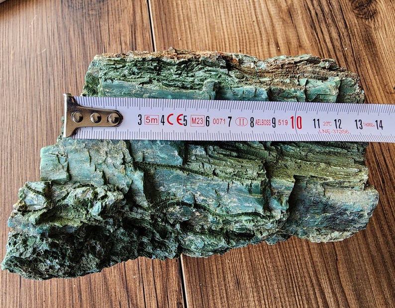 Op de afbeelding: Een stuk getextureerde, turquoise gekleurde schors met een meetlint eroverheen. De tape toont metingen in centimeters, waarbij de schors ongeveer 13 cm lang is.