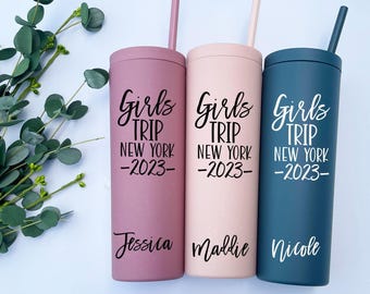 Pode incluir: Três copos cilíndricos altos em tons mate de malva, rosa claro e azul escuro, cada um com uma palhinha a condizer. Os copos apresentam o texto preto Girls TRIP NEW YORK 2023 e os nomes Jessica, Maddie e Nicole impressos na parte frontal.