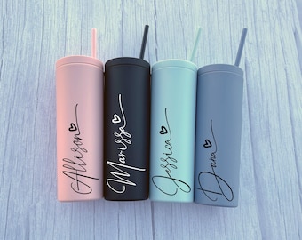May include: Four cylindrical tumblers with matching straws in pastel pink, matte black, light mint green, and slate blue. Each tumbler features a vertical script name in black ink, including Allison, Marissa, Jessica, and Dana, with a small heart icon.