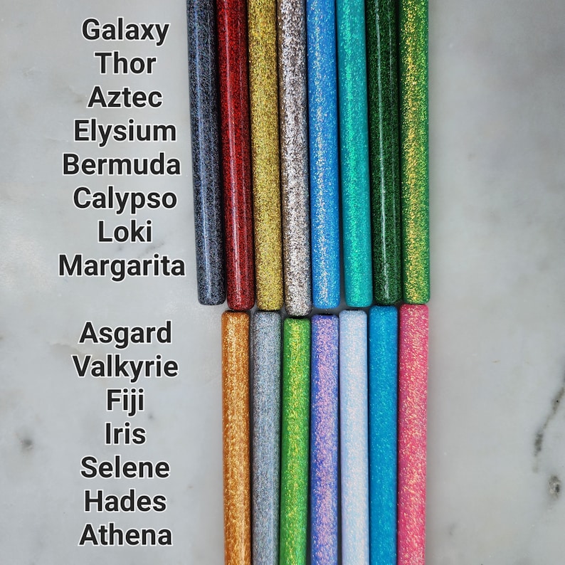 May include: A collection of 15 glitter-filled tubes, each with a different color and a name written below. The names include Galaxy, Thor, Aztec, Elysium, Bermuda, Calypso, Loki, Margarita, Asgard, Valkyrie, Fiji, Iris, Selene, Hades, and Athena.
