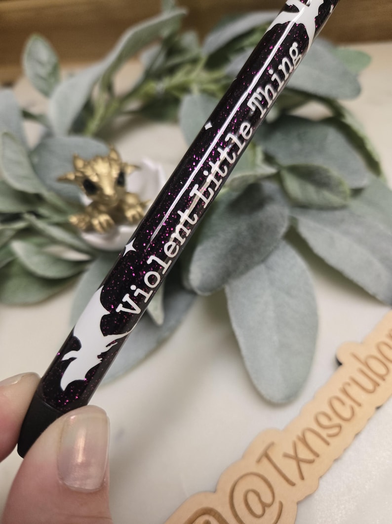 May include: A black and white pen with purple glitter and the text "Violent Little Thing" written in white on the side.