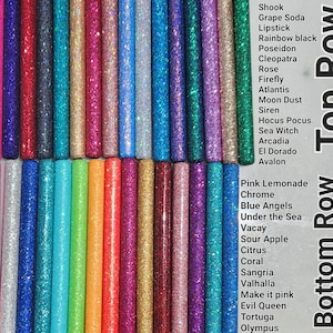 May include: A collection of glitter-filled glue sticks in various colors, arranged in two rows. The top row includes colors like Shook, Grape Soda, Lipstick, Rainbow Black, Poseidon, Cleopatra, Rose, Firefly, Atlantis, Moon Dust, Siren, Hocus Pocus, Sea Witch, Arcadia, El Dorado, and Avalon. The bottom row includes colors like Pink Lemonade, Chrome, Blue Angels, Under the Sea, Vacay, Sour Apple, Citrus, Coral, Sangria, Valhalla, Make it Pink, Evil Queen, Tortuga, and Olympus.