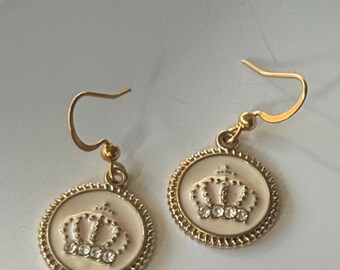 May include: A pair of gold dangle earrings with a white enamel circle featuring a gold crown with clear rhinestones.