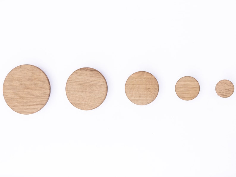 Puede incluir: Cinco ganchos de pared de madera de diferentes tama&ntilde;os, dispuestos en fila del m&aacute;s grande al m&aacute;s peque&ntilde;o. Los ganchos son circulares y de madera marr&oacute;n claro.