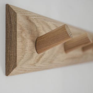 May include: A wooden wall-mounted coat rack with five rounded wooden hooks. The rack is made of light brown wood with a natural finish.
