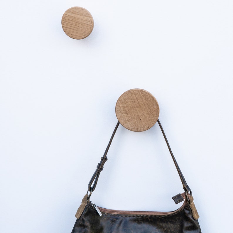 Puede incluir: Dos ganchos de pared de madera en forma de c&iacute;rculos, uno con un bolso de cuero marr&oacute;n colgado.