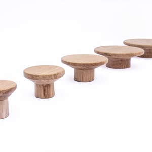 Puede incluir: Cinco pomos de madera de diferentes tama&ntilde;os, dispuestos en l&iacute;nea del m&aacute;s grande al m&aacute;s peque&ntilde;o. Los pomos son de color marr&oacute;n claro y tienen una parte superior redondeada y una base cil&iacute;ndrica.