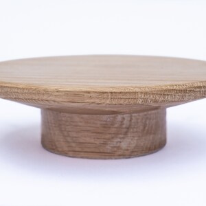Puede incluir: Un soporte para tartas de madera con una parte superior redonda y una base de pedestal. El soporte est&aacute; hecho de madera marr&oacute;n claro y tiene un acabado liso.