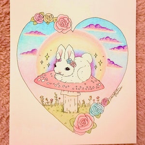 以下が含まれることがあります： ピンクの花を頭につけた白いウサギが、緑の茎のついた赤と白のキノコの上に座っています。キノコは緑の草とピンクと青の花に囲まれています。背景は虹と雲のあるハート型です。