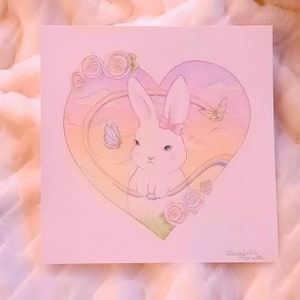 Puede incluir: Una ilustraci&oacute;n de acuarela de un conejo blanco con un lazo rosa, dentro de un marco en forma de coraz&oacute;n. El coraz&oacute;n est&aacute; lleno de un degradado de arco&iacute;ris y rodeado de flores. El texto "Intersgalactic Romantic" est&aacute; escrito en la esquina inferior derecha.