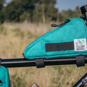 Op de afbeelding: Een turquoise fietstas met een zwarte band en een wit logo met de tekst "ELLUM BAG WORKS".