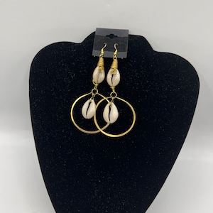 May include: Gold hoop earrings with a white seashell charm hanging from each hoop.