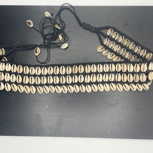 May include: A black cord belt with three rows of natural shell beads. The belt is tied with a long cord.