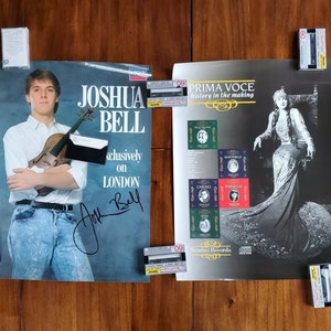 May include: Two posters, one featuring a young man holding a violin with the text "Joshua Bell" and "exclusively on London" and the other featuring a woman in a long gown with the text "Prima Voce history in the making" and "Nimbus Records".