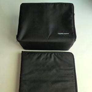 May include: Two black Case Logic carrying cases. The top case is rectangular and box-shaped, while the bottom case is flat and rectangular. Both cases have the Case Logic logo in white text.