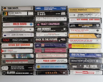 May include: A collection of vintage cassette tapes featuring various artists and albums, including Tom Waits, Miles Davis, Bob Dylan, Stevie Ray Vaughan, Public Enemy, and more. The tapes are arranged vertically in a stack, with the titles and artist names visible on the front of each tape.