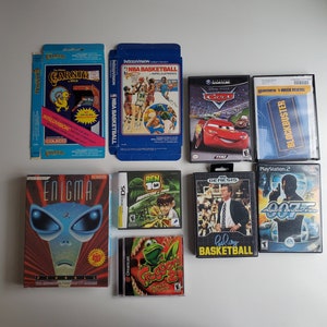 Può includere: Una collezione di cartucce e custodie di videogiochi retrò, tra cui titoli come "Carnival", "NBA Basketball", "Cars" e "007 Agent Under Fire". L'assortimento presenta varie piattaforme e generi di gioco, mostrando una nostalgica gamma di storia del gioco.