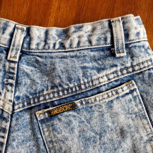 May include: A pair of light blue acid wash denim jeans with a back pocket and a small brown leather patch with the word "EIGSON" on it.