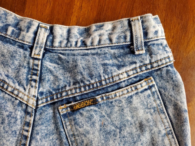 May include: A pair of light blue acid wash denim jeans with a back pocket and a small brown leather patch with the word "EIGSON" on it.
