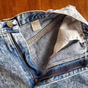 May include: A pair of light blue acid wash denim jeans with a zip fly and a button fastening. The jeans have a white tag inside the waistband that reads "T22W1127 SW 112 12".