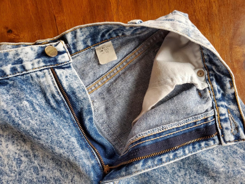May include: A pair of light blue acid wash denim jeans with a zip fly and a button fastening. The jeans have a white tag inside the waistband that reads "T22W1127 SW 112 12".